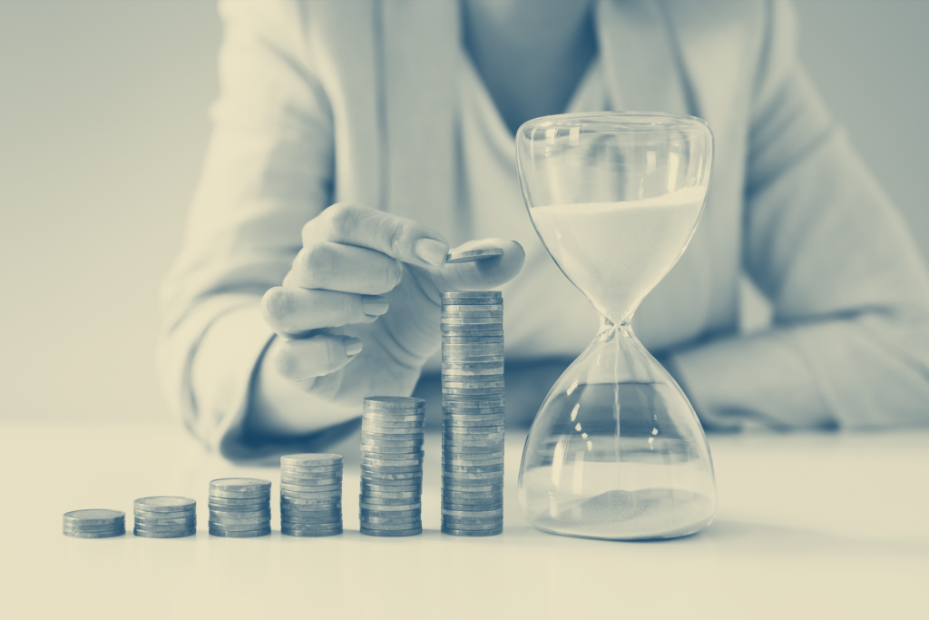 dollar-cost averaging concept image. Person stacking coins in short-to-tall rows from left to right next to an hour glass.
